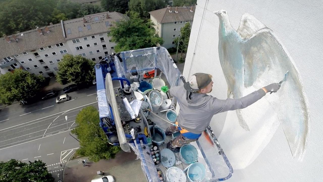 ein Mann malt in großer Höhe auf einer Hausfassade