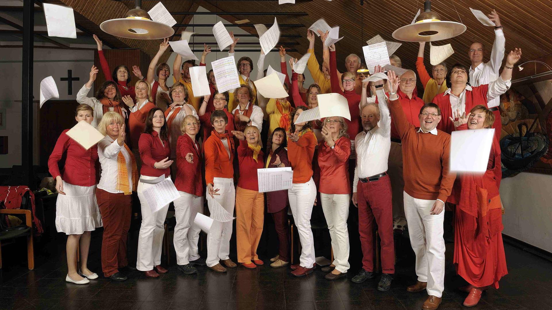 Gruppenfoto des Chors Lampenfieber aus Bergisch-Gladbach. Die Sängerinnen und Sänger werfen Notenblätter in die Luft.