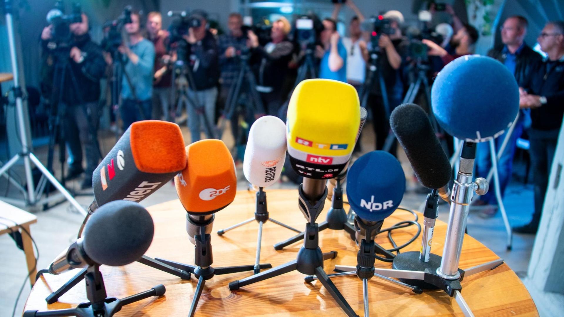 Bei einer Pressekonferenz sind Mikrofone auf einem Tisch platziert und Kameras aufgebaut. Bei einer Pressekonferenz sind Mikrofone auf einem Tisch platziert und Kameras aufgebaut.