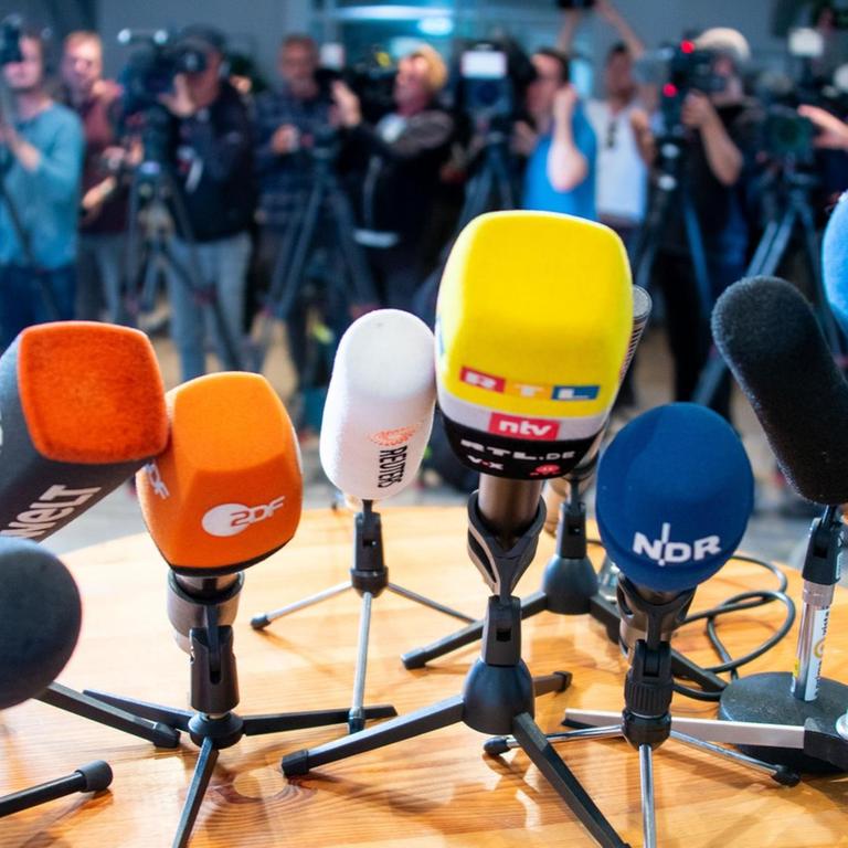 Bei einer Pressekonferenz sind Mikrofone auf einem Tisch platziert und Kameras aufgebaut.