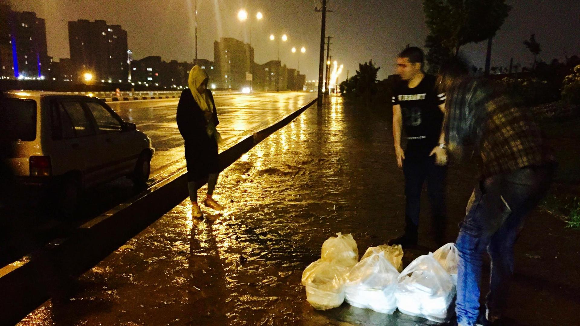 Sie sehen eine Stadtautobahn in Teheran im Regen, drei Menschen stehen dort, und ein Auto. Sie sehen eine Stadtautobahn in Teheran im Regen, drei Menschen stehen dort, und ein Auto.