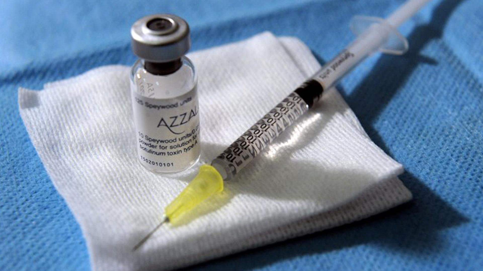 Auf einem blauen Tuch liegen auf weißen Tüchern eine Botox-Ampulle und eine Spritze parat. Auf einem blauen Tuch liegen auf weißen Tüchern eine Botox-Ampulle und eine Spritze parat.