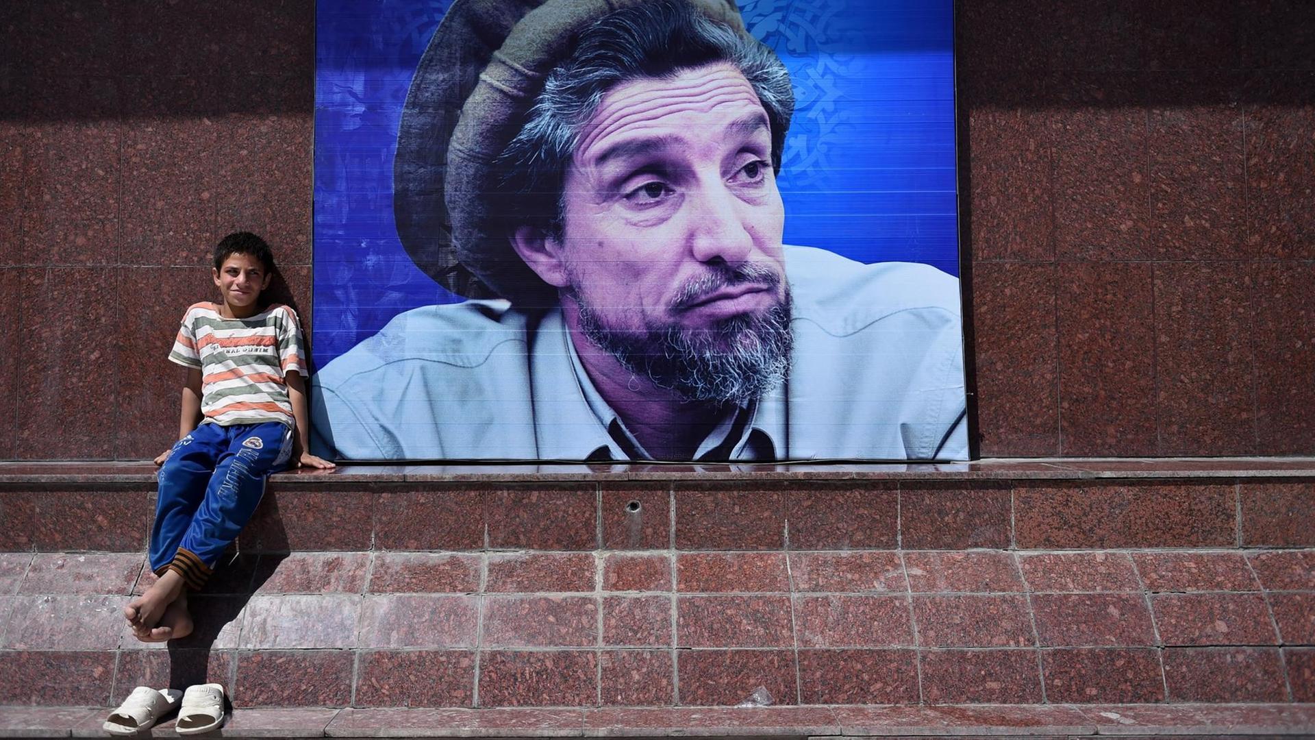 Ein afghanischer Junge sitzt neben einem Plakat mit dem Bild des verstorbenen Widerstandsführers Ahmad Shah Massoud