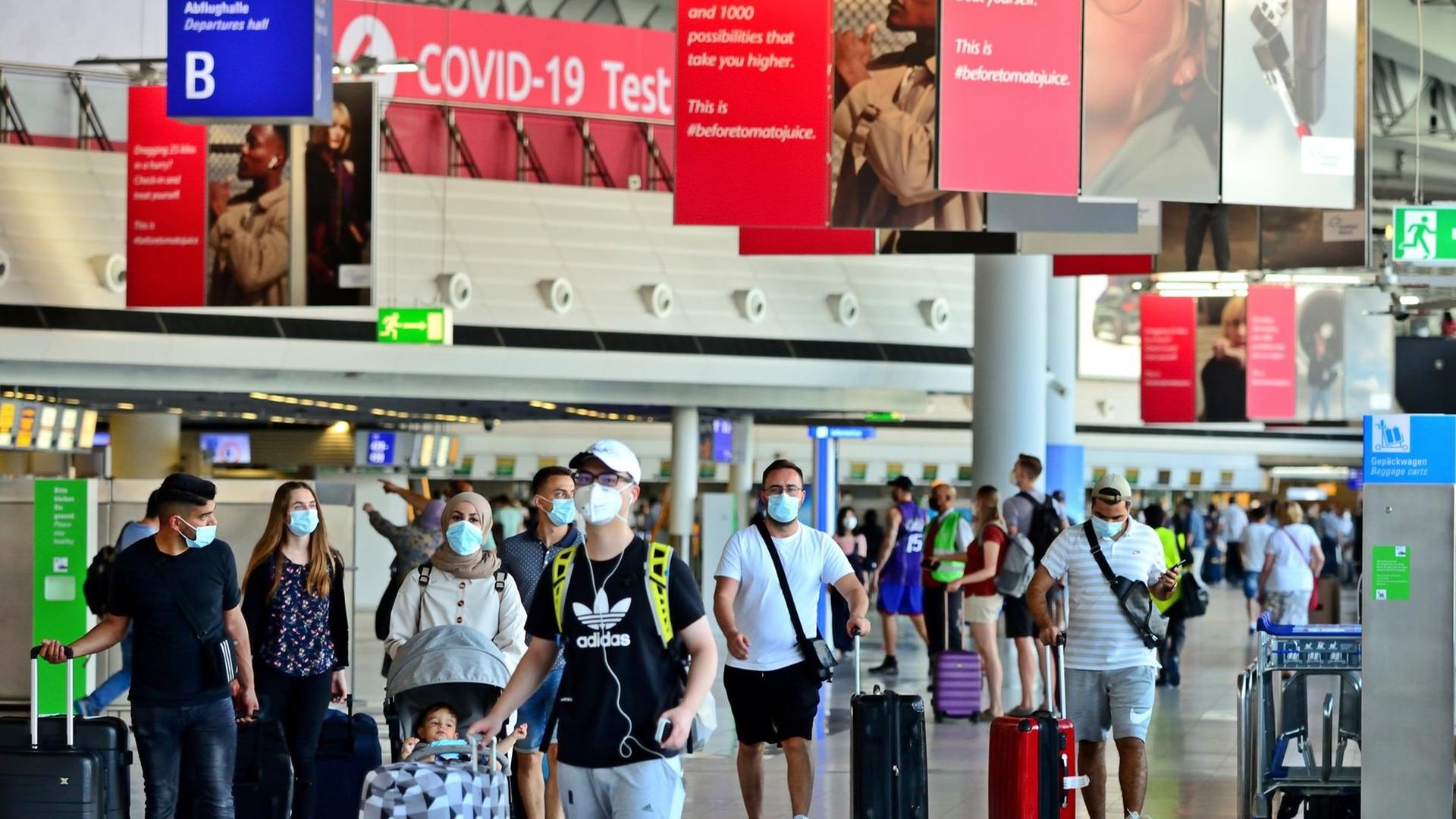 Reisende am Flughafen Frankfurt, im Hintergrund ist ein Schild zu sehen mit der Aufschrift "Covid-19-Test".
