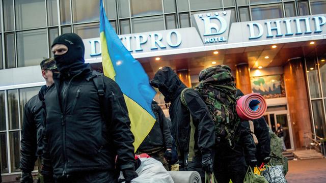 Eine Reihe von Männern, zum Teil vermummt oder mit Kaputzen, steht mit Koffern in der ukrainischen Hauptstadt Kiew.