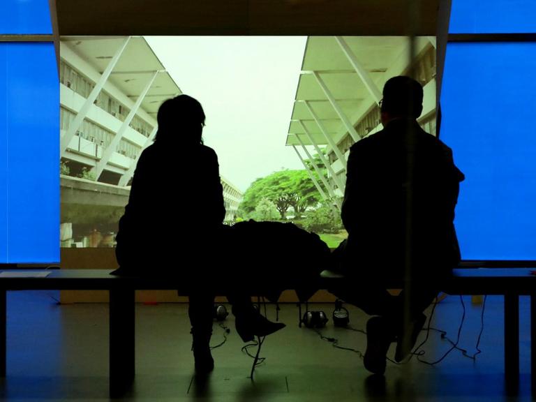 Die Ausstellung "Bauhaus Imaginista" im Berliner Haus der Kulturen der Welt. Zwei Besucher sitzen vor einer Leinwand oder einem Bildschirm und schauen sich eine Installation an.