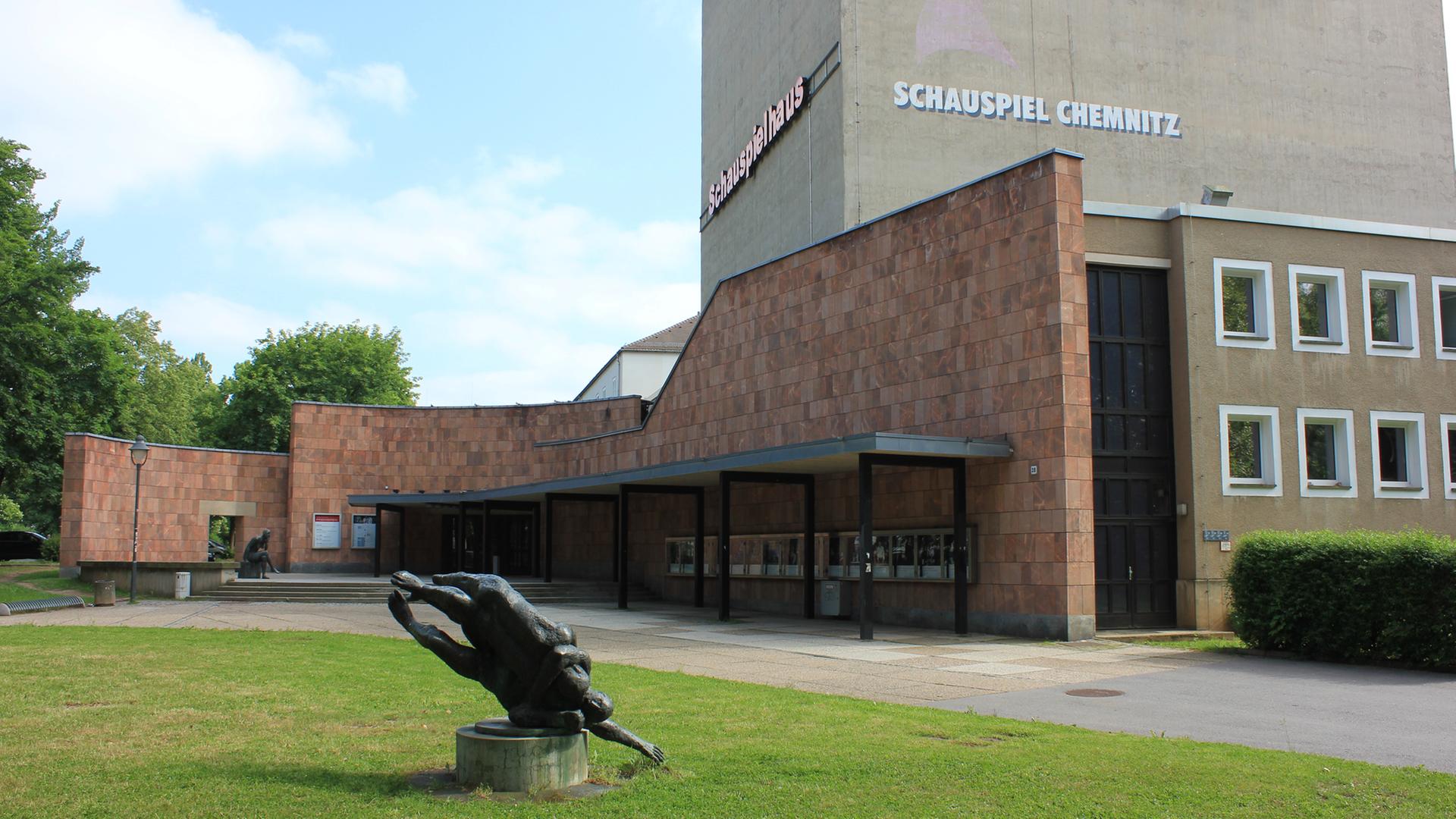 Eine Statue auf einer grünen Wiese vor einem Gebäude, auf dem "Schauspiel Chemnitz" steht Eine Statue auf einer grünen Wiese vor einem Gebäude, auf dem "Schauspiel Chemnitz" steht