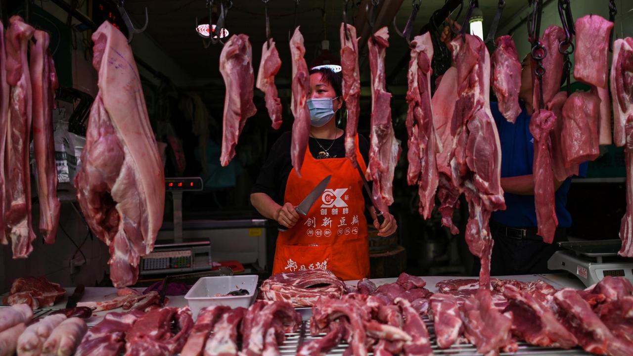 Eine Fleischverkäuferin steht mit dem Messer in der Hand hinter ihren Fleischauslagen.