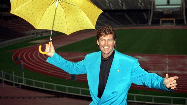 Der amerikanische Popstar David Hasselhoff präsentiert sich lächelnd mit einem gelben Regenschirm am 20.02.1993 im Berliner Olympiastadion.