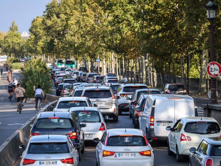 Blick auf eine Straße in Paris: rechts fahren Autos, links fahren Menschen auf Fahrrädern auf einem Radweg