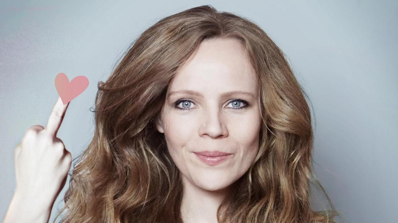 Porträt der Kabarettistin Sarah Bosetti, sie zeigt den Mittelfinder, auf dessen Spitze ist ein Herz Porträt der Kabarettistin Sarah Bosetti, sie zeigt den Mittelfinder, auf dessen Spitze ist ein Herz
