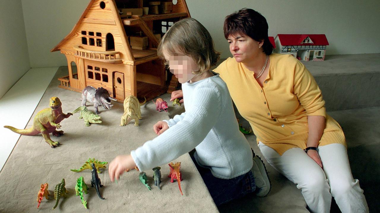 Ein Mädchen spielt unter Aufsicht einer Therapeutin mit Figuren in einer Kinderschutzambulanz.