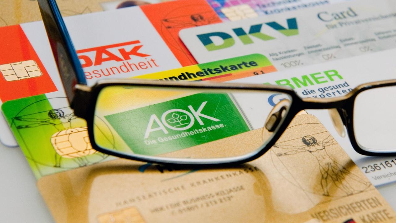 Die Chipkarten verschiedener Krankenkassen liegen am Dienstag (14.08.2012) in Berlin unter einer Brille nebeneinander auf einem Tisch. Die Chipkarten verschiedener Krankenkassen liegen am Dienstag (14.08.2012) in Berlin unter einer Brille nebeneinander auf einem Tisch.