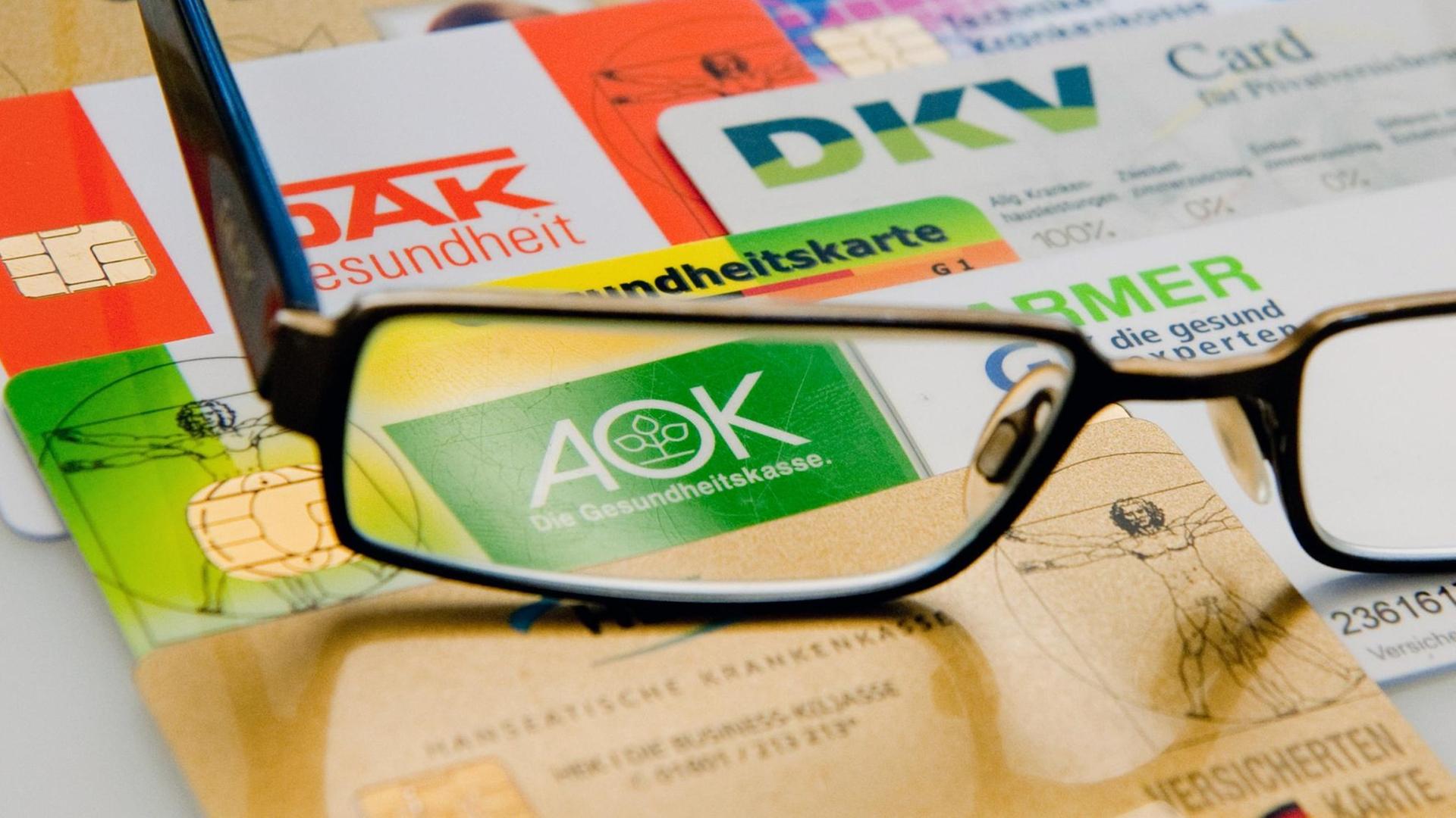 Die Chipkarten verschiedener Krankenkassen liegen am Dienstag (14.08.2012) in Berlin unter einer Brille nebeneinander auf einem Tisch. Die Chipkarten verschiedener Krankenkassen liegen am Dienstag (14.08.2012) in Berlin unter einer Brille nebeneinander auf einem Tisch.