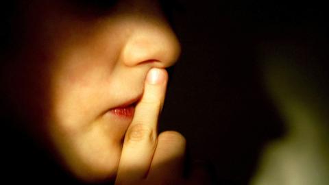 Ein Junge hält sich einen Finger vor den geschlossenen Mund.
