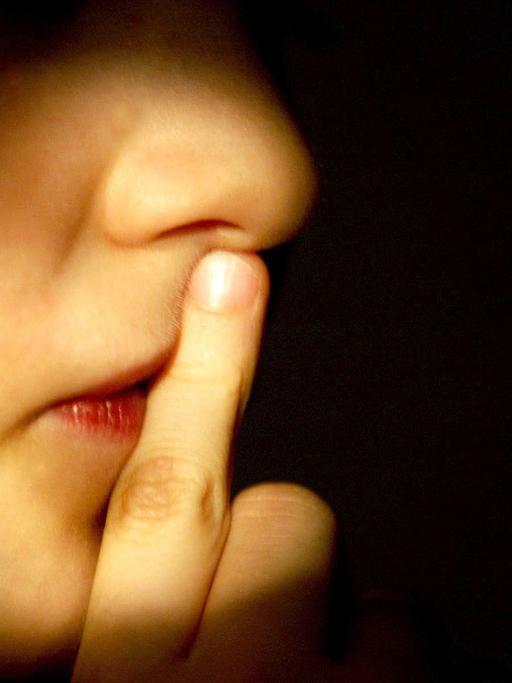 Ein Junge hält sich einen Finger vor den geschlossenen Mund.