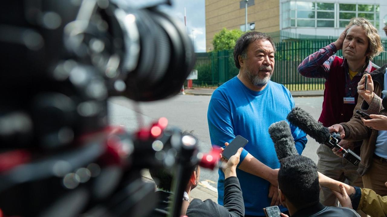 Ai Weiwei steht in betont legerer Kleidung außerhalb eines Gefängnisses, umringt von Journalisten.