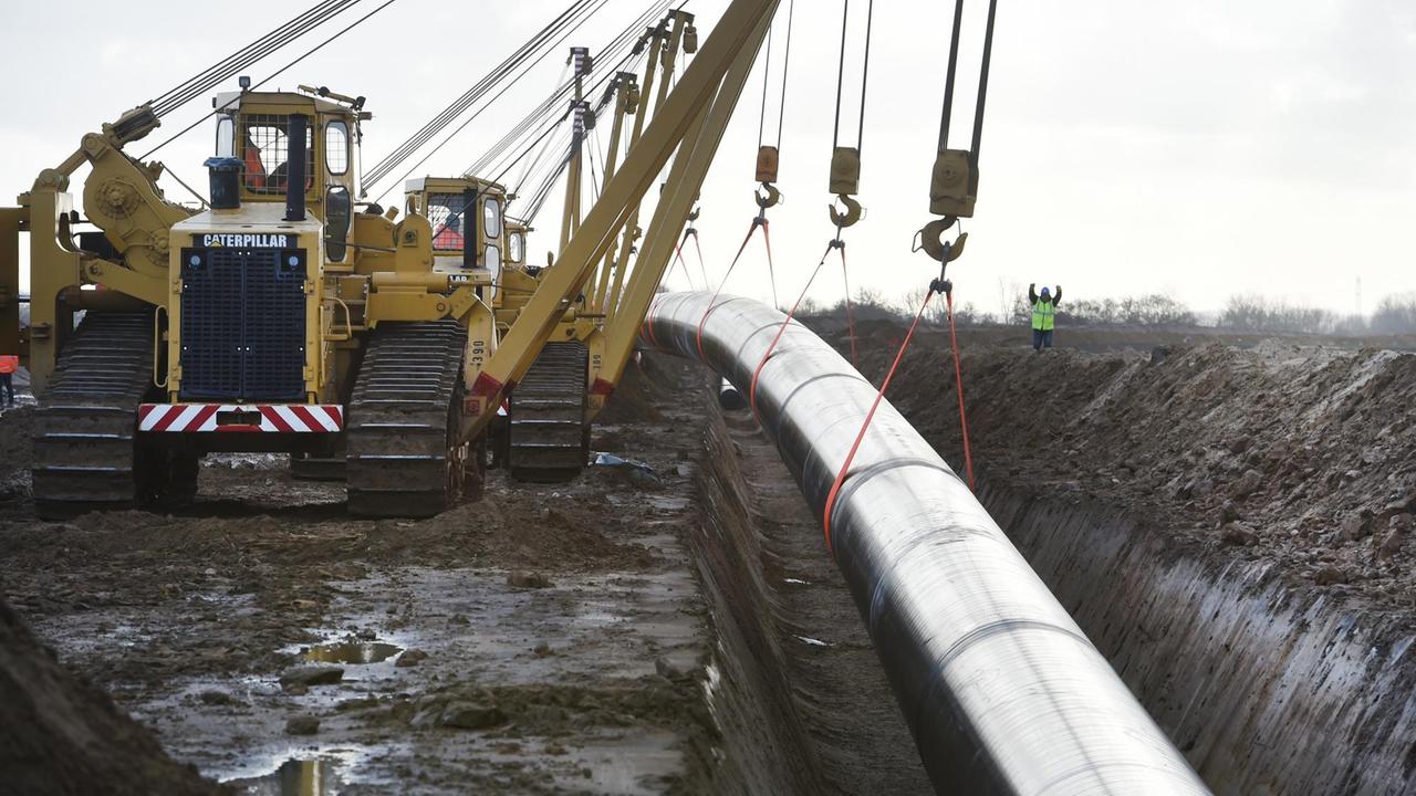 Ein Pipeline-Stück der Erdgaspipeline Eugal wird mit Hilfe von Seitenbaumkränen bei Anklam ins Erdreich verlegt.