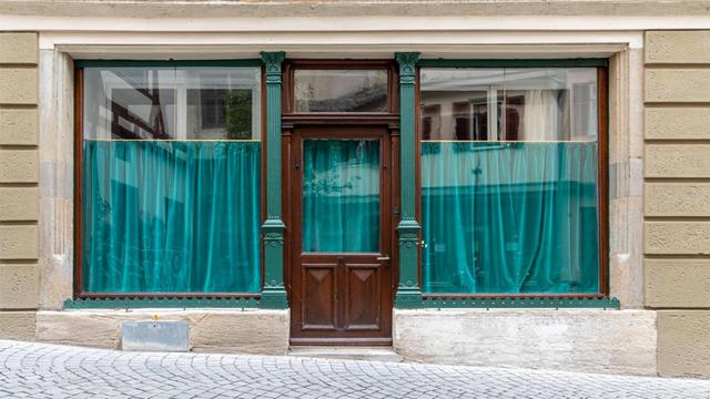Leeres Ladengeschäft mit geschlossenen, türkisfarbenen Vorhängen im Schaufenster, in der Innenstadt von Tübingen.