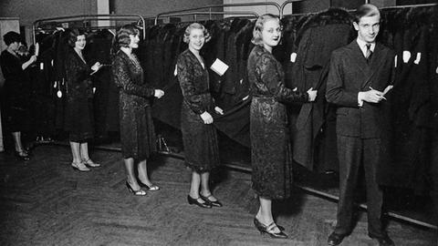 Elegante Mitarbeiterinnen des Konfektionsunternehmens Leopold Seligmann am Hausvogteiplatz in Berlin posieren vor Kleiderstangen mit angefertigter Mode.