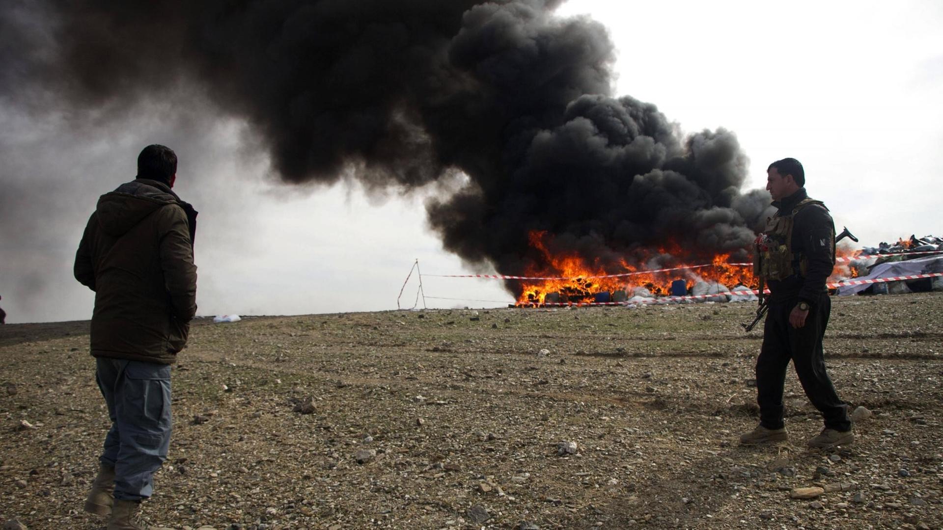 Dunkle Rauchwolken von einem Feuer ziehen über ein staubiges Feld, auf dem zwei Männer stehen. Dunkle Rauchwolken von einem Feuer ziehen über ein staubiges Feld, auf dem zwei Männer stehen.