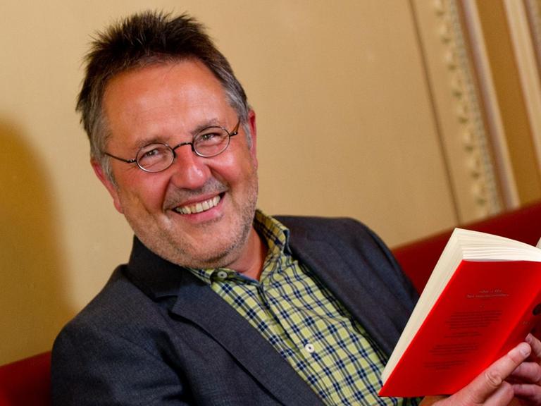 Zu sehen ist der Leiter des Hamburger Literaturhauses, Rainer Moritz, der ein rotes Buch aufgeschlagen in den Händen hält.