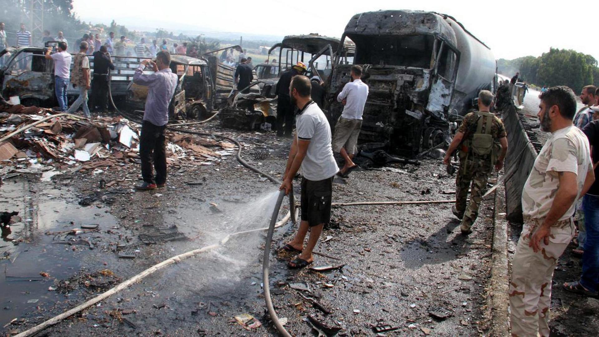 Syrische Soldaten und Zivilisten zwischen ausgebrannten Bussen und Autos nach einem Bombenanschlag des IS bei Tartus