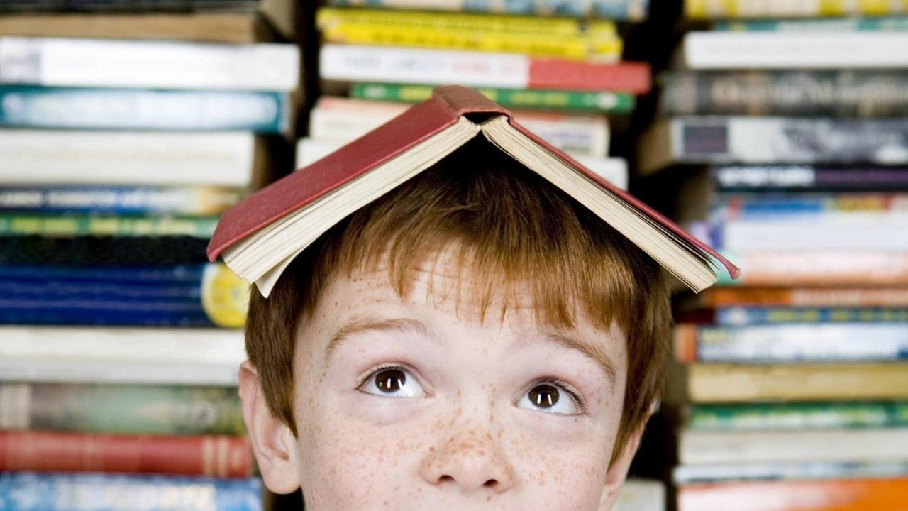 Ein rothaariger Junge mit einem Buch auf dem Kopf. Ein rothaariger Junge mit einem Buch auf dem Kopf.