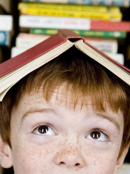 Ein rothaariger Junge mit einem Buch auf dem Kopf.
