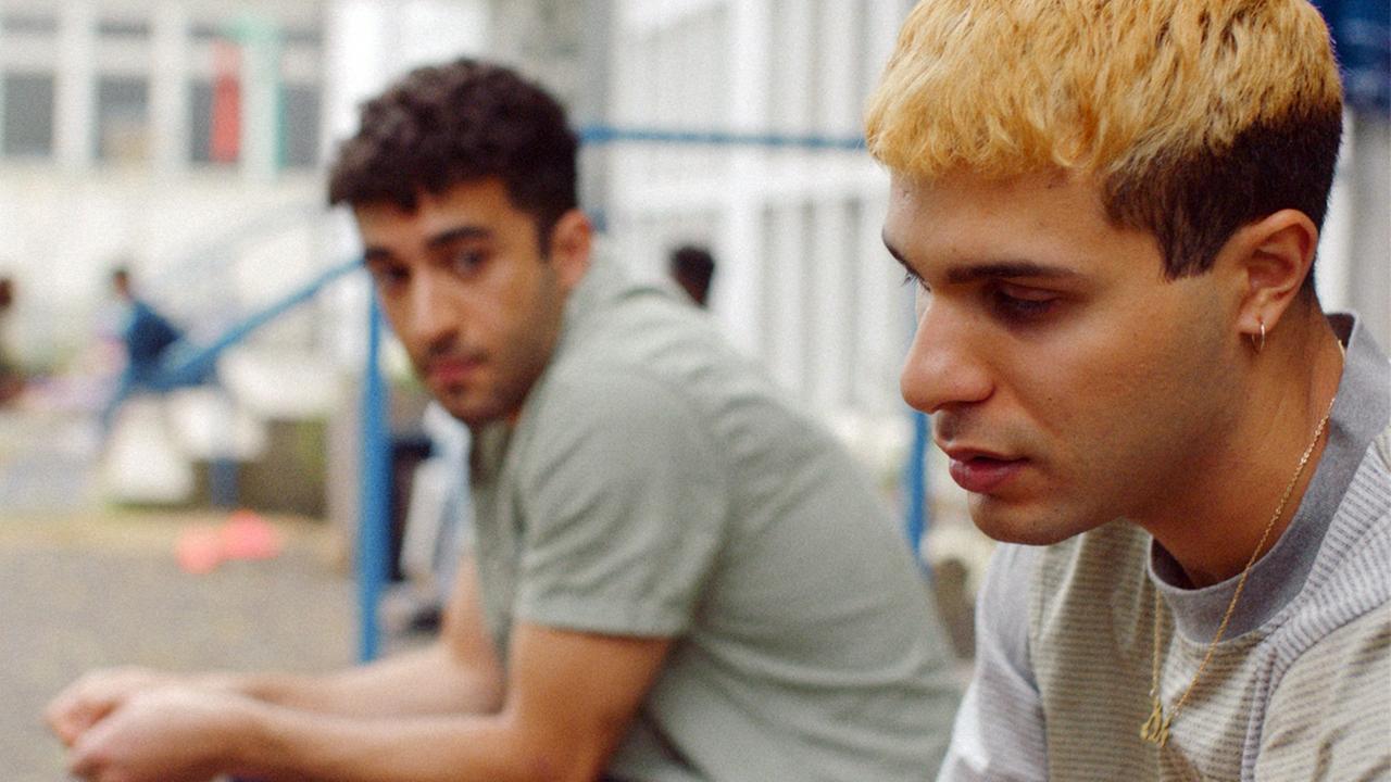 Filmstill aus "Futur Drei": Zwei Männer sitzen nebeneinander auf Stufen. Filmstill aus "Futur Drei": Zwei Männer sitzen nebeneinander auf Stufen.