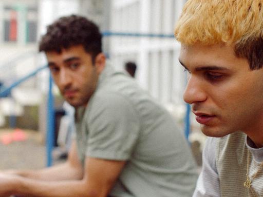 Filmstill aus "Futur Drei": Zwei Männer sitzen nebeneinander auf Stufen.