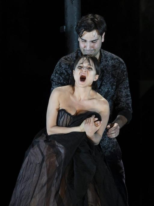 Eine Probenaufnahme von Berry Koskys Inszenierung von Giacomo Puccinis "La Bohème" zeigt im Bühnendunkel die Sängerin der Rolle der Mimi in üppigen Kleid , dramatisch singend in den Armen eines bleichen Rodolfo