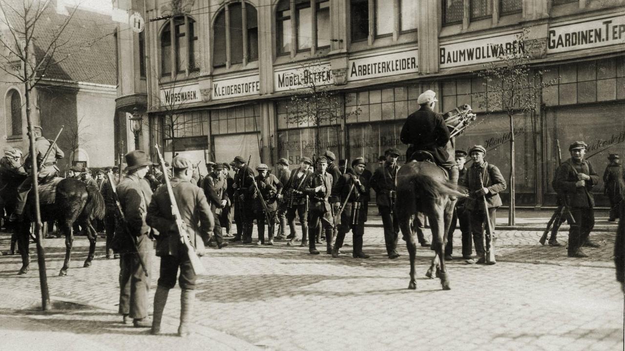Schwarz-weiß-Foto von 1920: Auf einer Straße sammeln sich Arbeiter.