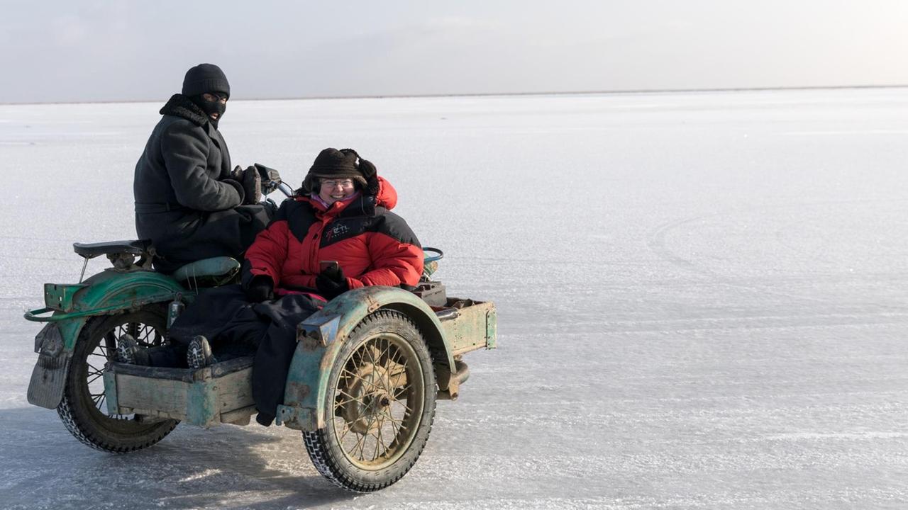 Edda Schlager mit Fischern unterwegs auf dem Aralsee. Sie sitzt im Seitenwagen des Mopeds. Der See ist gefrohren.