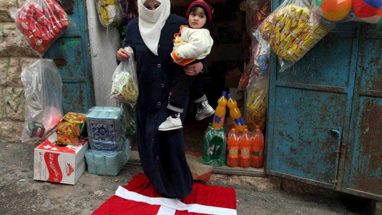 Eine Frau in Hebron trägt ihr Kind und ihre Einkäufe über eine dänische Fahne. Eine Frau in Hebron trägt ihr Kind und ihre Einkäufe über eine dänische Fahne.