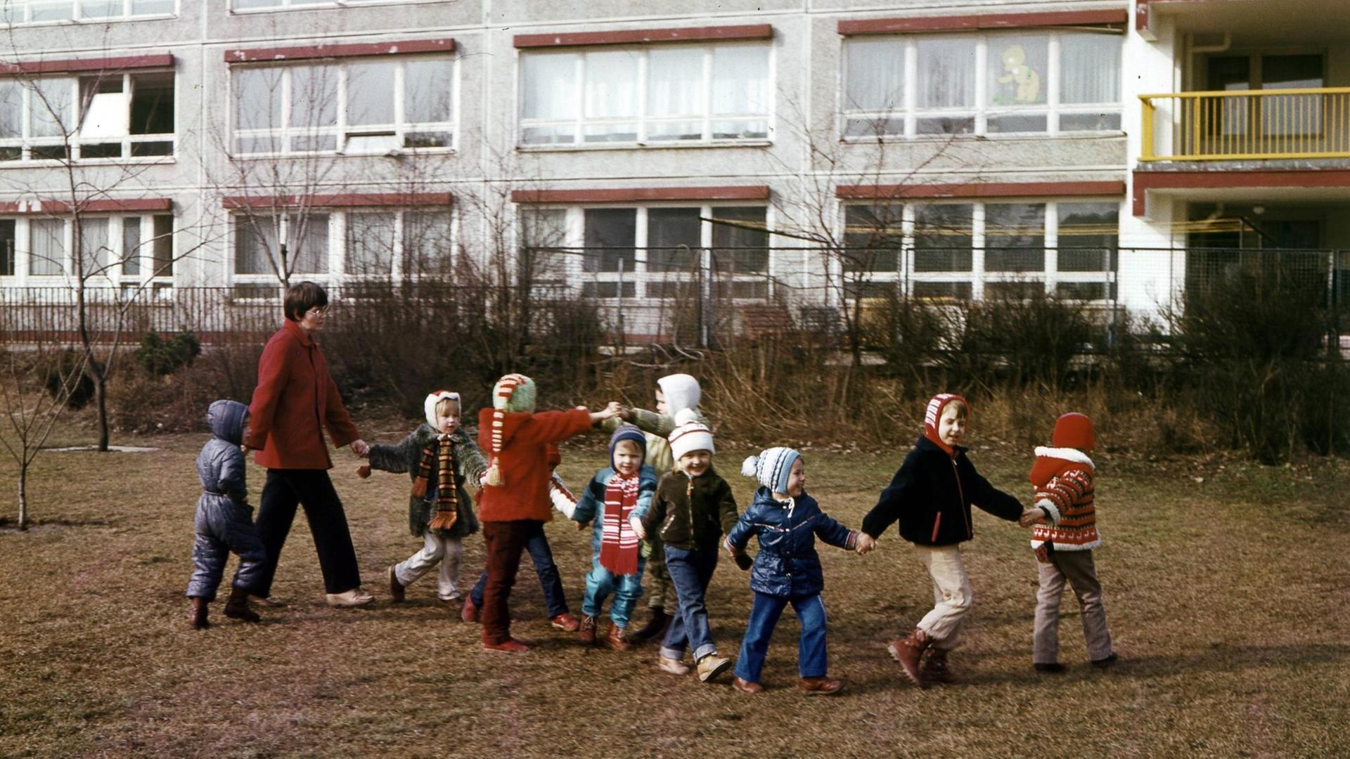 Historische Farbfotografie von Kindergartenkindern und einer Erzieherin, die sich alle an den Händen halten