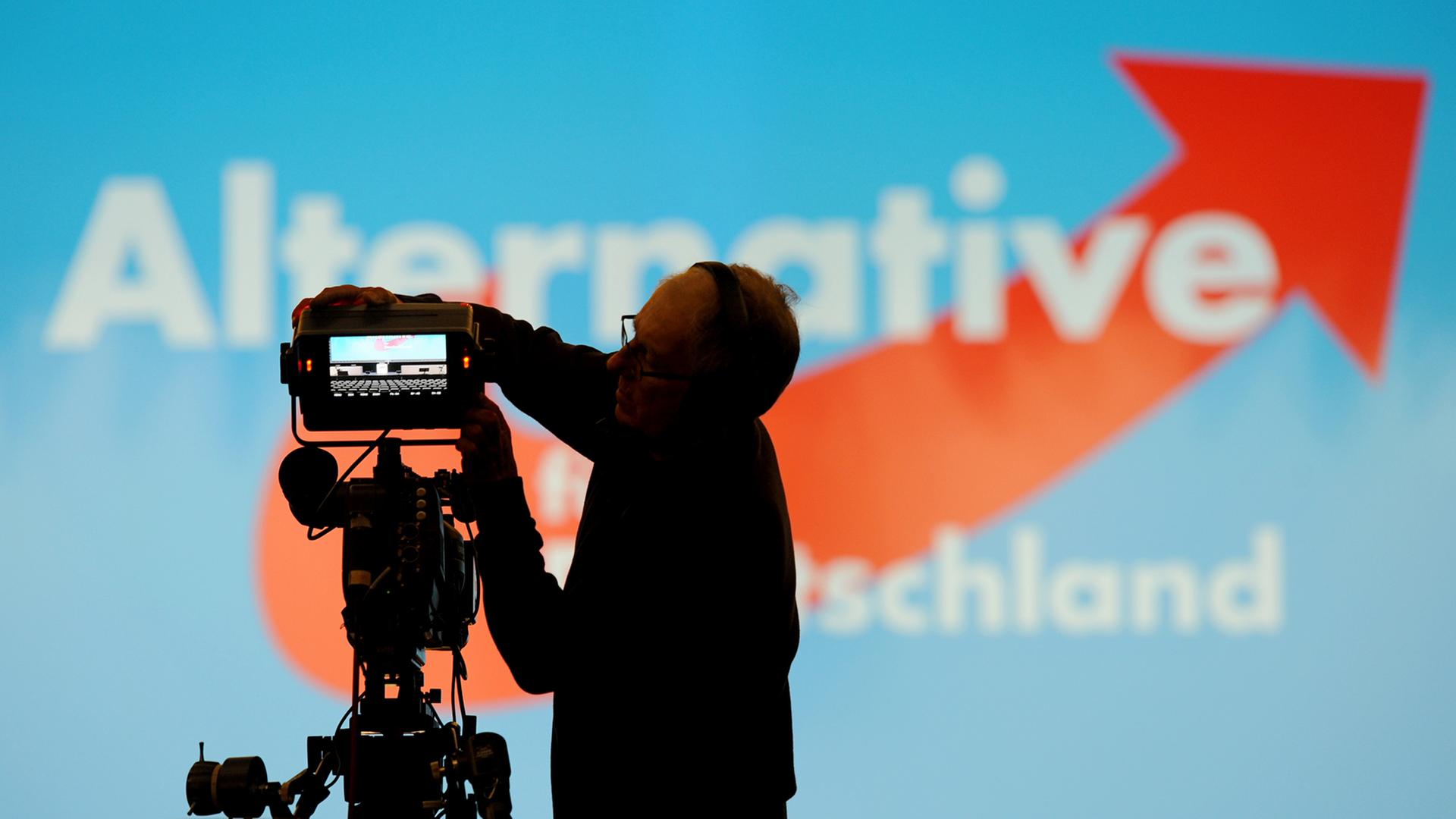 Ein Kameramann baut vor einer Wand mit dem Logo der Partei Alternative für Deutschland (AfD) eine Kamera auf. Ein Kameramann baut vor einer Wand mit dem Logo der Partei Alternative für Deutschland (AfD) eine Kamera auf.