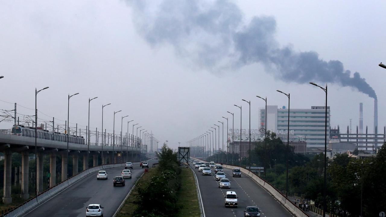 Eine stark befahrene Schnellstraße in Neu Delhi in Indien führt an einer Fabrik mit rauchendem Schlot vorbei. Das Bild ist blaustichig, der Himmel grau. Das Foto wurde wohl von einer Brücke aus aufgenommen. Eine stark befahrene Schnellstraße in Neu Delhi in Indien führt an einer Fabrik mit rauchendem Schlot vorbei. Das Bild ist blaustichig, der Himmel grau. Das Foto wurde wohl von einer Brücke aus aufgenommen.