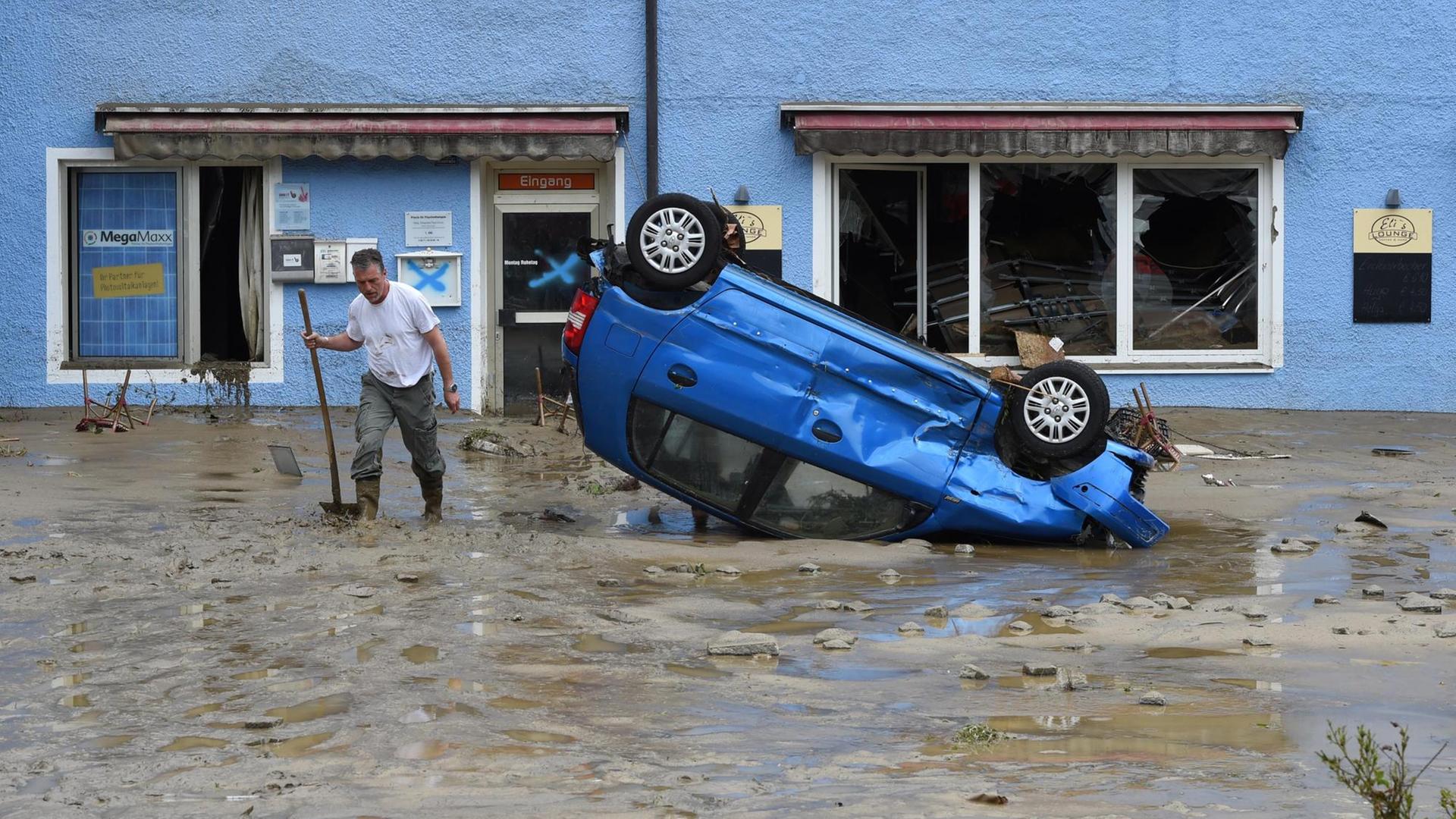 Ein Einwohner des Ortes Simbach am Inn in Bayern steht im Hochwasser-Gebiet auf einer überfluteten Straße neben einem beschädigten Auto, das auf dem Dach liegt. Ein Einwohner des Ortes Simbach am Inn in Bayern steht im Hochwasser-Gebiet auf einer überfluteten Straße neben einem beschädigten Auto, das auf dem Dach liegt.
