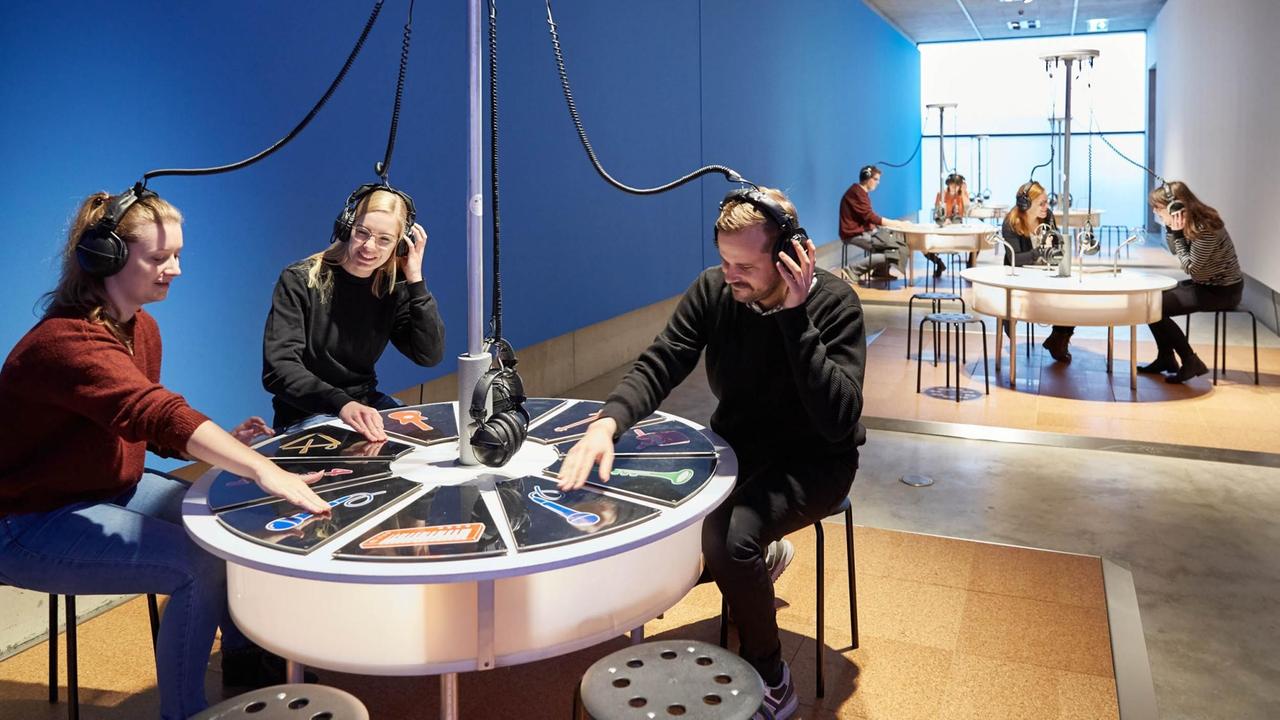 Museumsbesucher der Ausstellung "Music" in Bonn sitzen an Tischen und probieren aus
