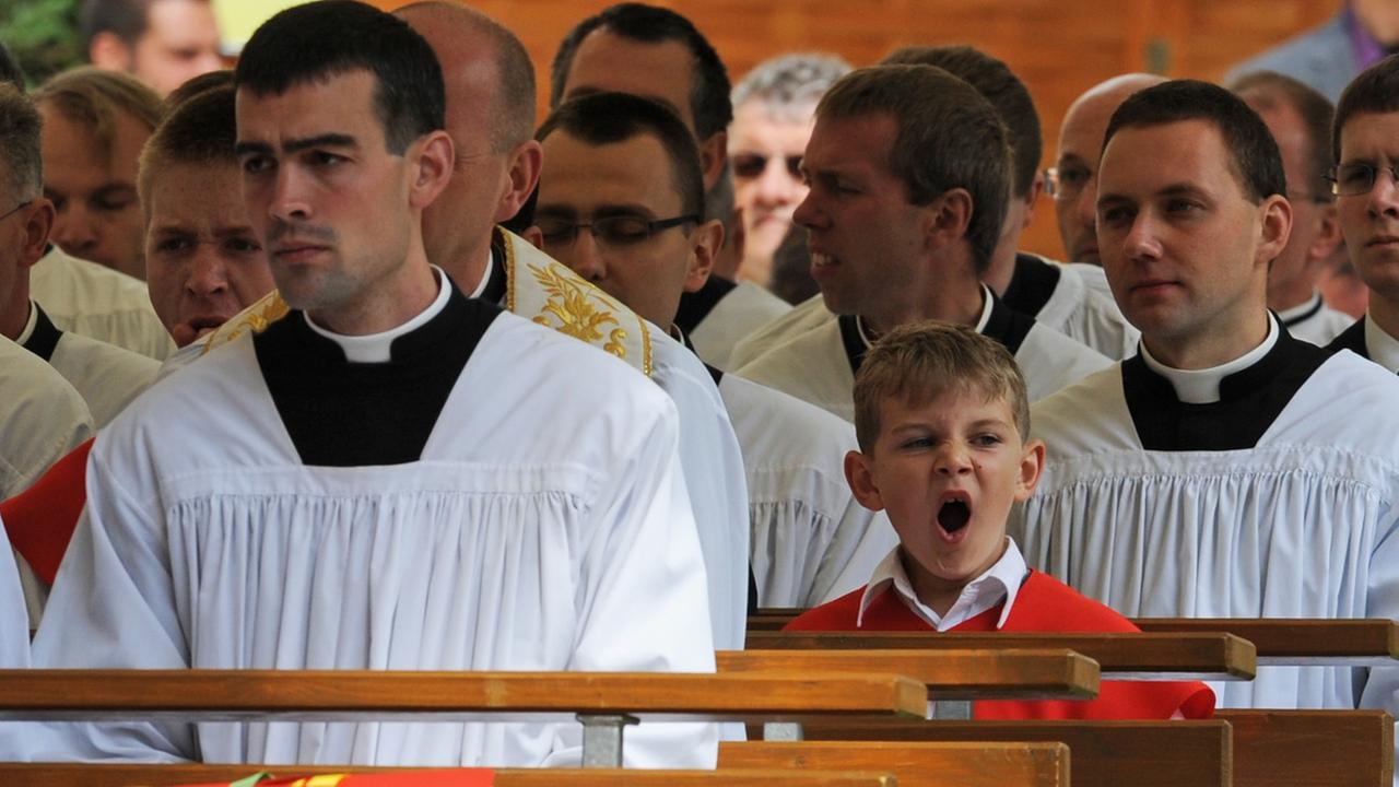 Ein kleiner Junge gähnt am Samstag  im Priesterseminar der Piusbruderschaft in Zaitzkofen  während der Priesterweihe zwischen Geistlichen.  Foto: Armin Weigel / dpa