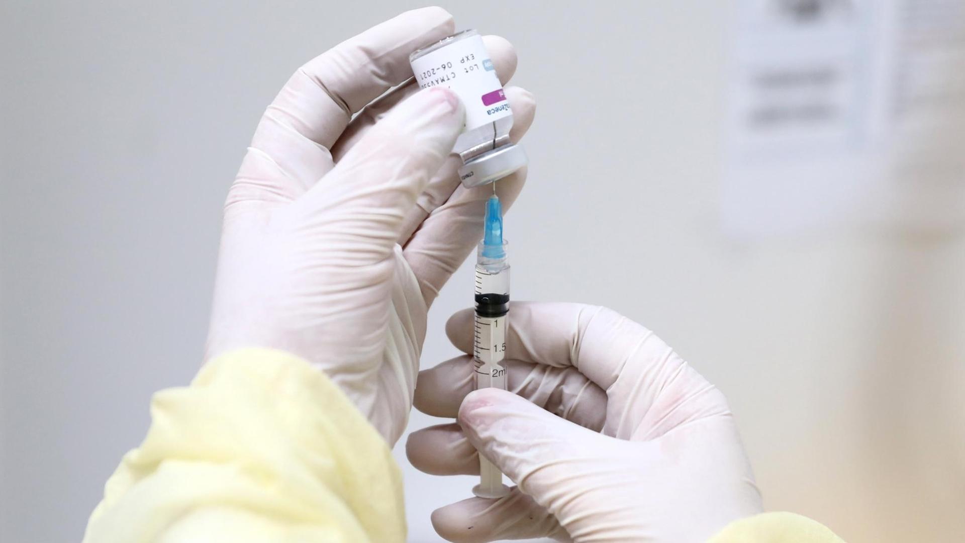 Medizinisches Personal hält eine Spritze mit dem Imfpstoff von Astrazeneca in den Händen. Spritze und Ampulle sind halb verdeckt. Die Person trägt weiße Latexhandschuhe. Medizinisches Personal hält eine Spritze mit dem Imfpstoff von Astrazeneca in den Händen. Spritze und Ampulle sind halb verdeckt. Die Person trägt weiße Latexhandschuhe.