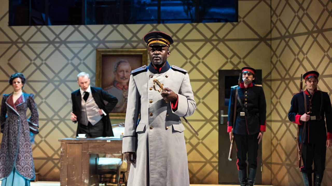 Ouelgo Téné als Hauptmann von Köpenick am Landestheater Altenburg Theater & Philharmonie Thüringen Der Hauptmann von Köpenick Ein deutsches Märchen von Carl Zuckmayer Premiere, 26.2.17. Wilhelm Voigt: Ouelgo Téné (vorn) Erster Soldat: Johannes Emmrich (rechts) Obermüller: Manuel Kressin Frau Obermüller: Anne Diemer Zweiter Soldat: Yasin Baig. Ouelgo Téné als Hauptmann von Köpenick am Landestheater Altenburg Theater & Philharmonie Thüringen Der Hauptmann von Köpenick Ein deutsches Märchen von Carl Zuckmayer Premiere, 26.2.17. Wilhelm Voigt: Ouelgo Téné (vorn) Erster Soldat: Johannes Emmrich (rechts) Obermüller: Manuel Kressin Frau Obermüller: Anne Diemer Zweiter Soldat: Yasin Baig.