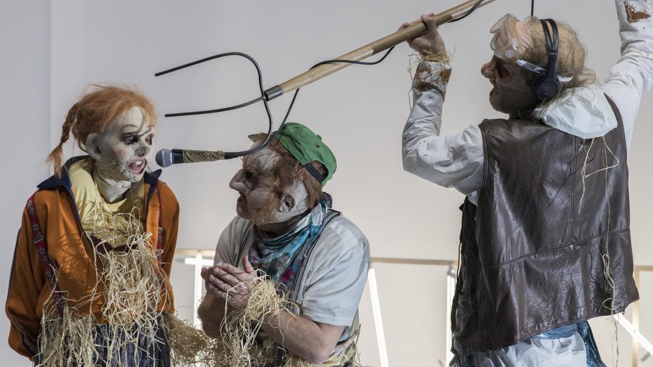 Szene aus der Inszenierung "Farm Fatale" an den Münchner Kammerspielen. Zu sehen sind (v.l.n.r.) die Schauspieler Julia Riedler, Stefan Merki, Gaëtan Vourc'h. Einer der Schauspieler hält eine Mistgabel in den Händen.