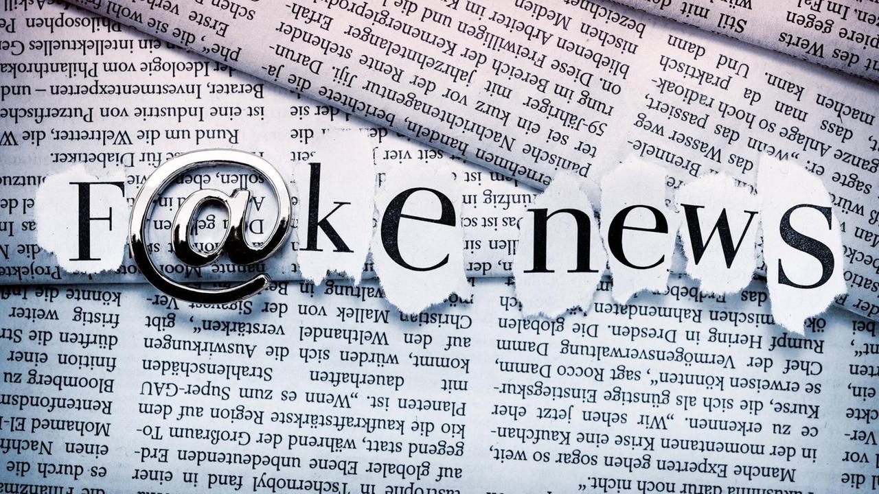 Schriftzug Fake News mit At-Zeichen auf gestapelten Zeitungen. Schriftzug Fake News mit At-Zeichen auf gestapelten Zeitungen.