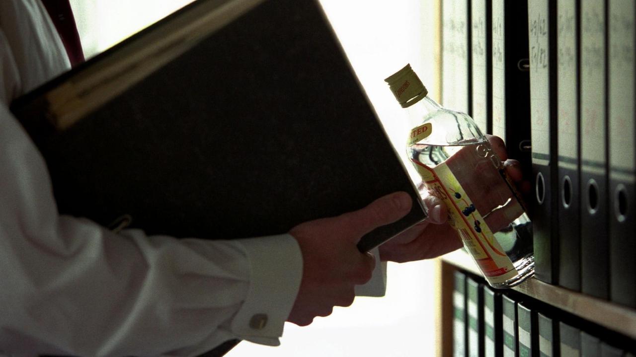 Symbolfoto zum Thema " Alkohol am Arbeitsplatz ": Ein Mann holt heimlich hinter Aktenordnern eine Flasche Gin hervor. Symbolfoto zum Thema " Alkohol am Arbeitsplatz ": Ein Mann holt heimlich hinter Aktenordnern eine Flasche Gin hervor.