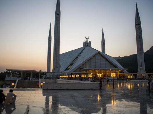 Besucher der Faisal-Moschee in der pakistanischen Hauptstadt Islamabad sitzen bei Sonnenuntergang auf dem Vorplatz der Moschee.