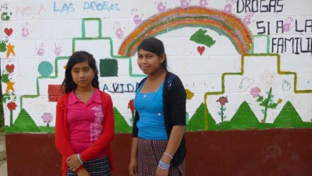 Zwei guatemaltekische Mädchen stehen vor einer bemalten Wand.