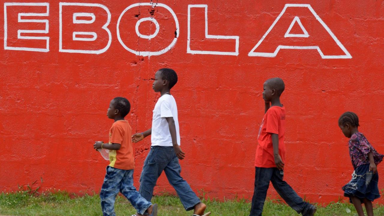 Vier Kinder im Schulkindalter laufen vor einer knallroten Mauer mit der weißen Aufschrift "Ebola". Vier Kinder im Schulkindalter laufen vor einer knallroten Mauer mit der weißen Aufschrift "Ebola".