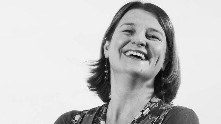 Prof. Nathalie Singer. Frau Singer steht lachend mit verschränkten Armen dem Fotografen zugewandt. Das Foto ist in schwarz-weiß Prof. Nathalie Singer. Frau Singer steht lachend mit verschränkten Armen dem Fotografen zugewandt. Das Foto ist in schwarz-weiß